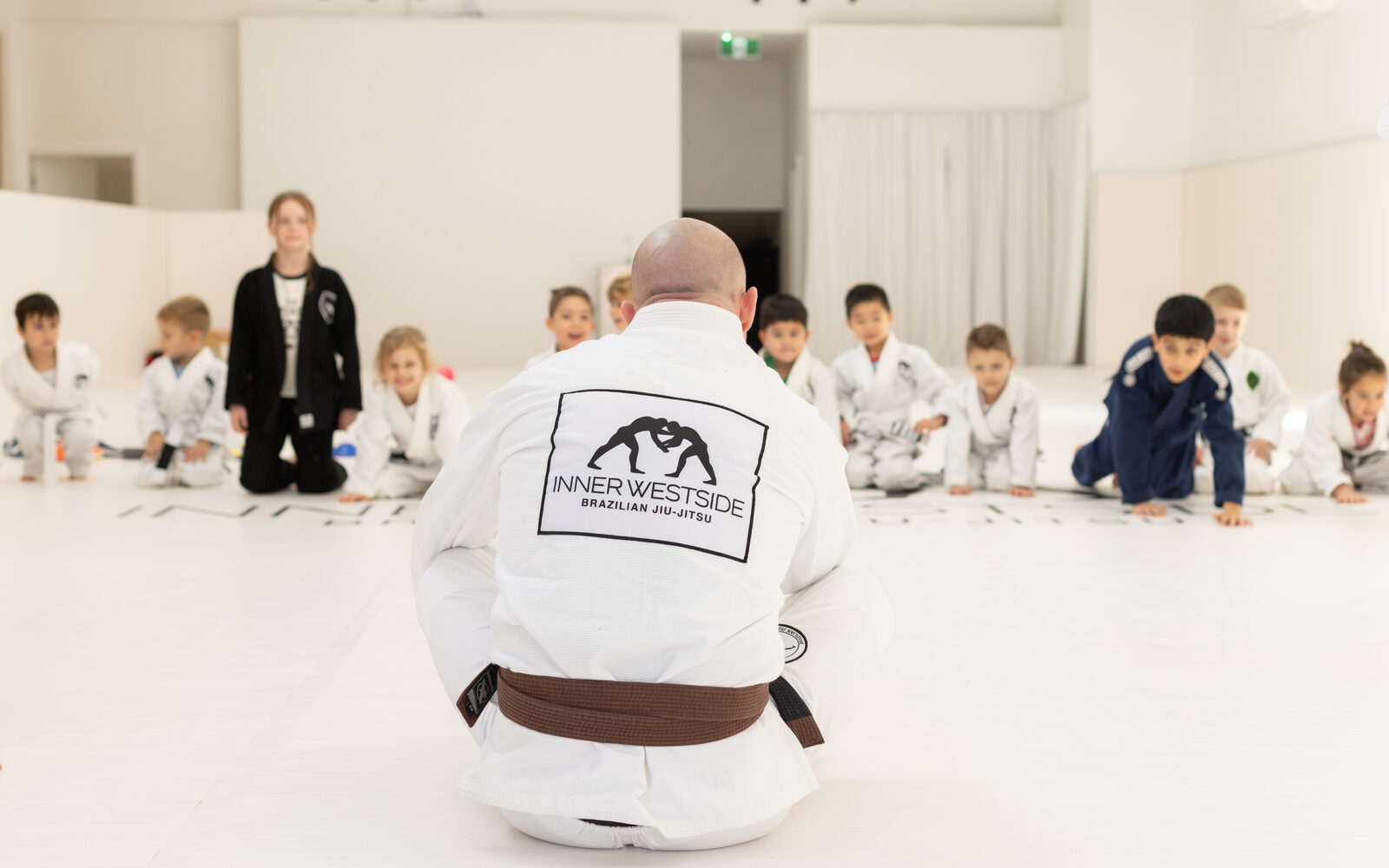 Coach John-Henry Mallam kneeling in front of the kids class at the start of a session
