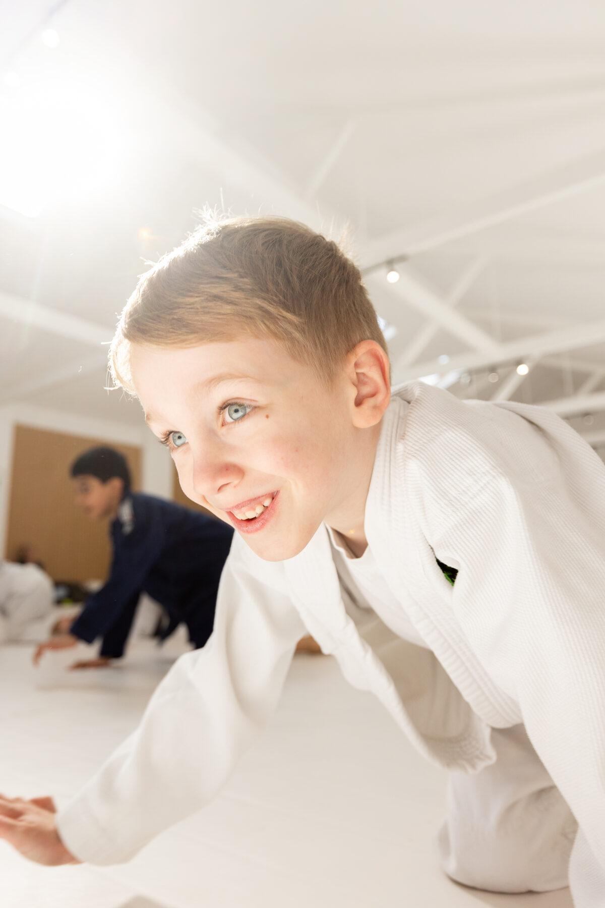 A boy in a white gi smiling during a kids class movement drill