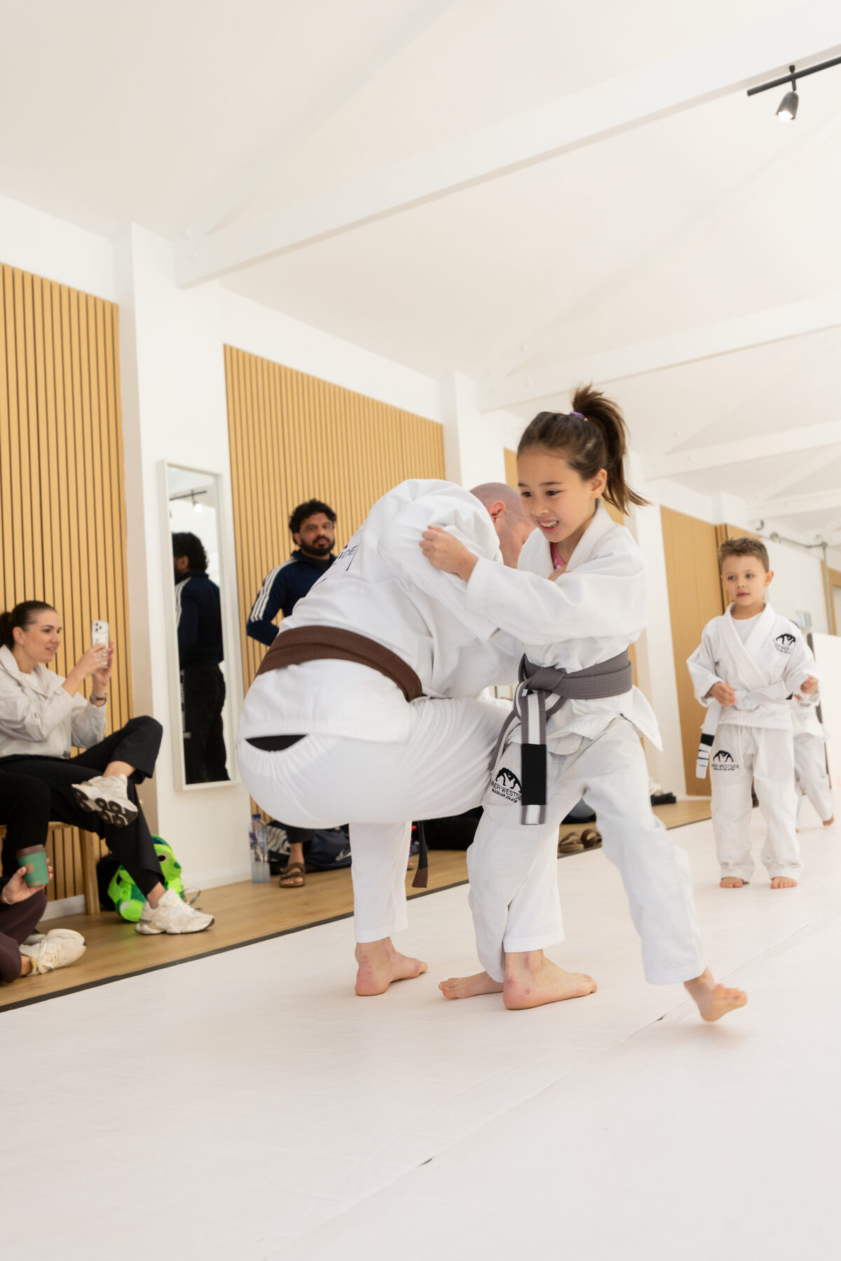 Coach John-Henry Mallam practising a takedown with a young student while parents watch