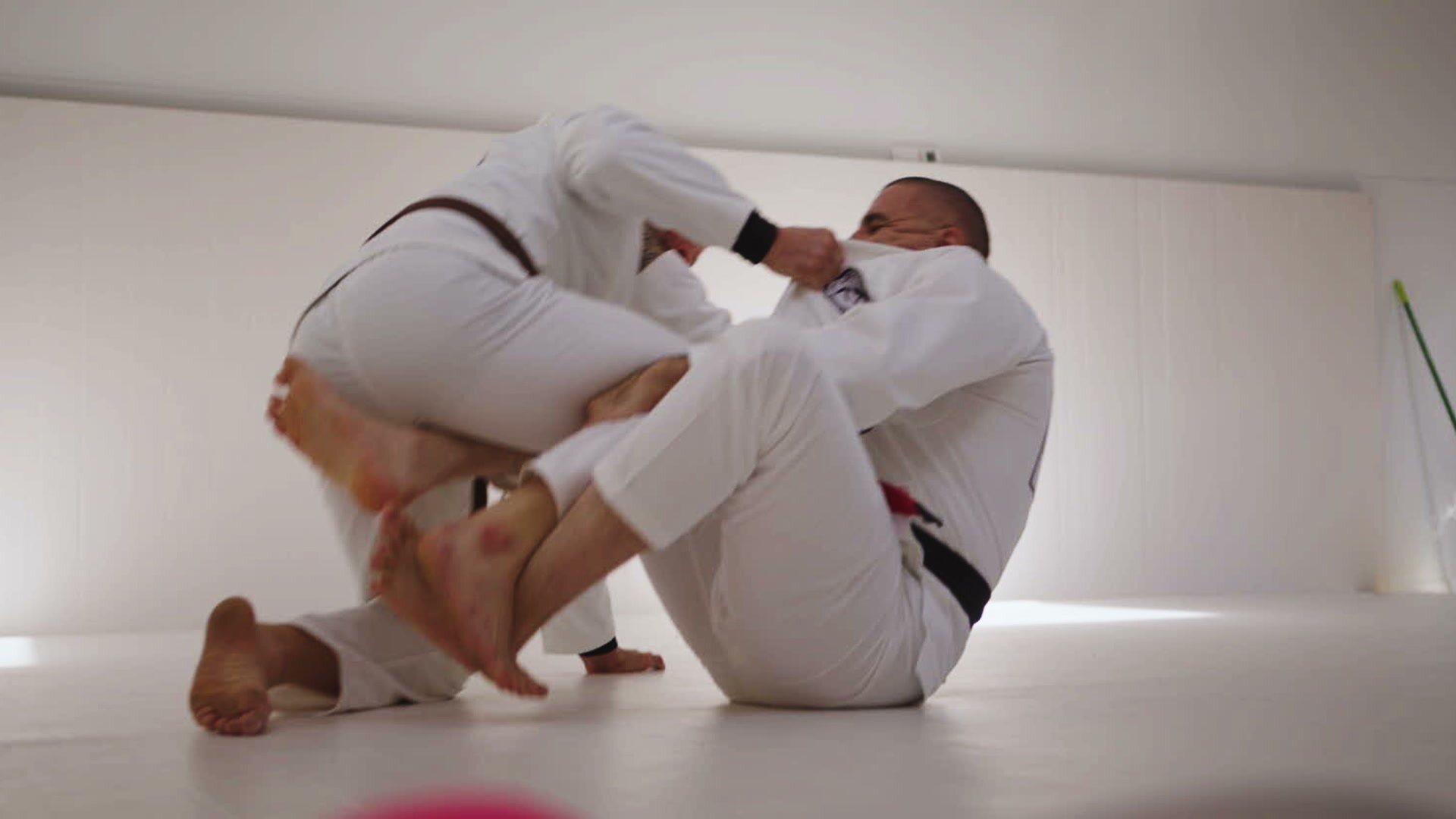 Two members rolling in white gis on the mats at Inner Westside BJJ